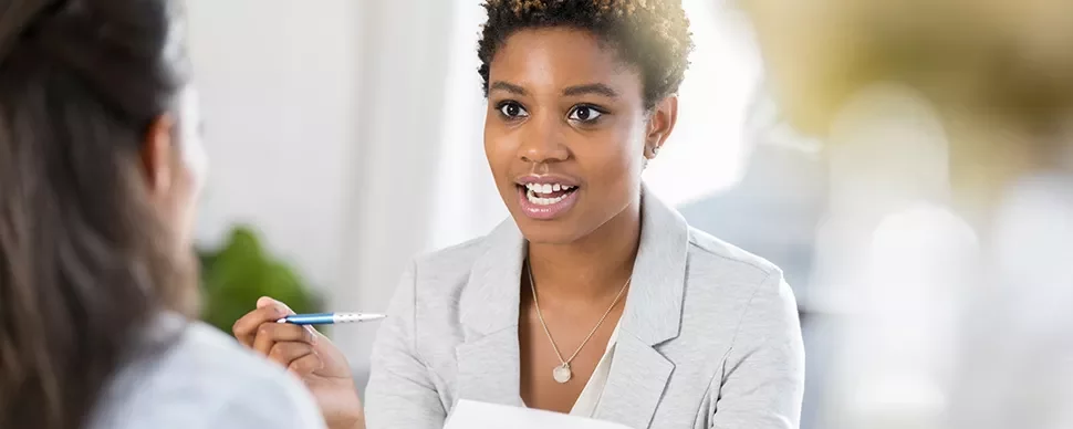 Woman in a gray suit holding a pen, engaged in conversation.