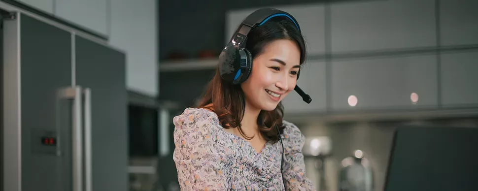 Smiling woman in headphones working on a laptop in a modern kitchen.