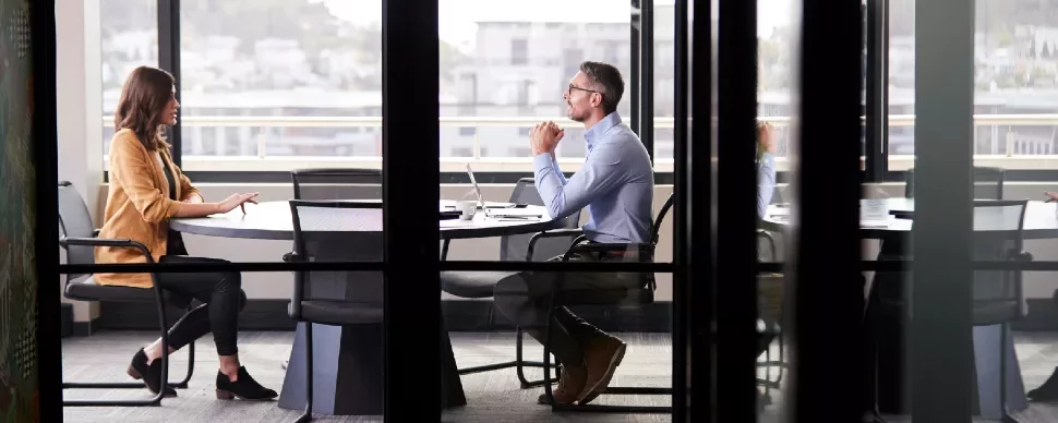 Two people having a meeting in a glass-walled office.