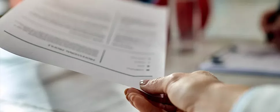 Close-up of a person's hand holding a document over a table.