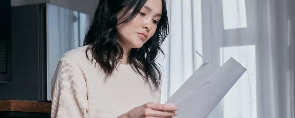Woman in a white sweater reading a document while sitting indoors.