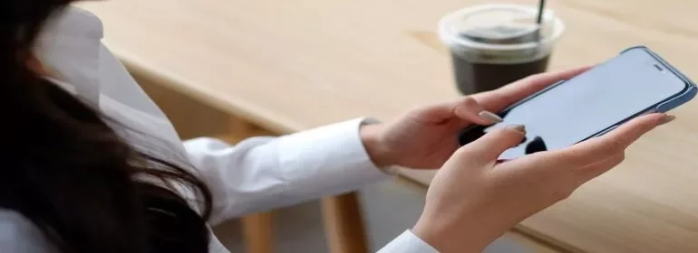 A woman sitting at a table, focused on her cell phone, with a relaxed expression on her face.