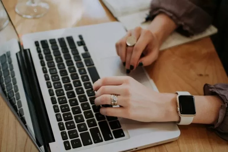 A woman typing on a laptop, wearing a watch on her wrist, focused on her work.
