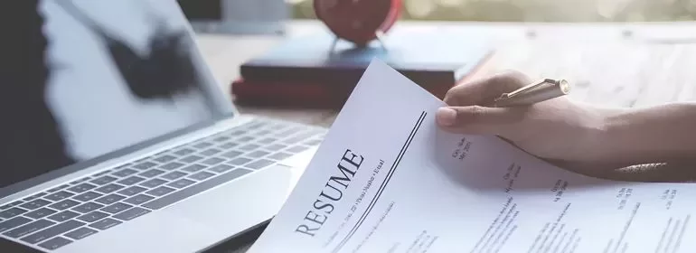 A person holding a resume in front of a work device