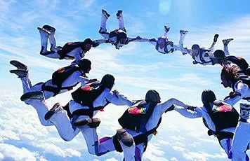 Group of skydivers forming a circle in the sky against a backdrop of clouds on a sunny day.