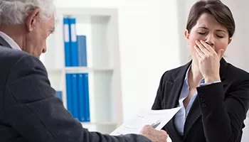 Two people in an office, one holding papers, the other yawning.