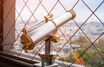 Telescope overlooking city view through lattice fence.