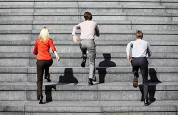 Three people in business attire running up a large set of stairs.