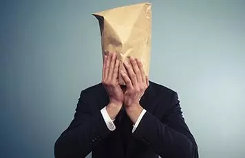 Person in a suit with a paper bag over their head, against a plain background.