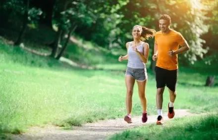 A man and woman jogging on a sunny path surrounded by green trees.