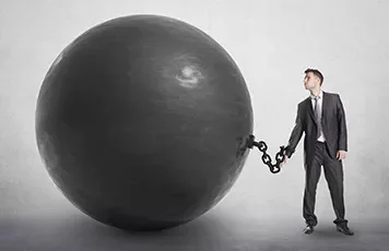 Man in business suit chained to a large black ball.