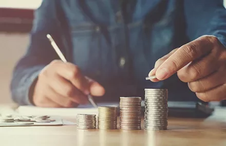 Person stacking coins in ascending order on a desk, emphasizing savings and financial planning.