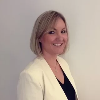 Portrait of a smiling woman with short blonde hair in a white blazer.