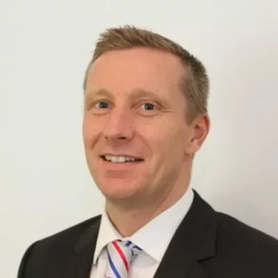 Smiling man in a business suit with a striped tie against a plain background.