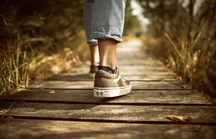 Person walking on a wooden path in nature, wearing casual sneakers and jeans.