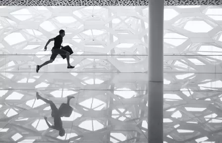 Silhouette of a man running indoors with a patterned wall reflection on the shiny floor.