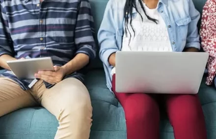 Two people sitting on a sofa with a tablet and a laptop.