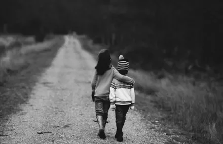 Two children walking on a rural path, one with an arm around the other, in black and white.