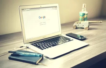 Laptop with Google search on screen, placed on a desk with a phone and notebook.