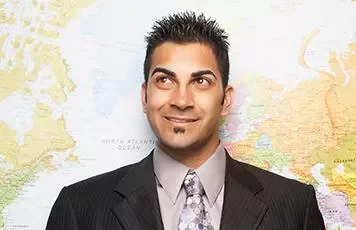 Smiling man in a suit stands in front of a world map.