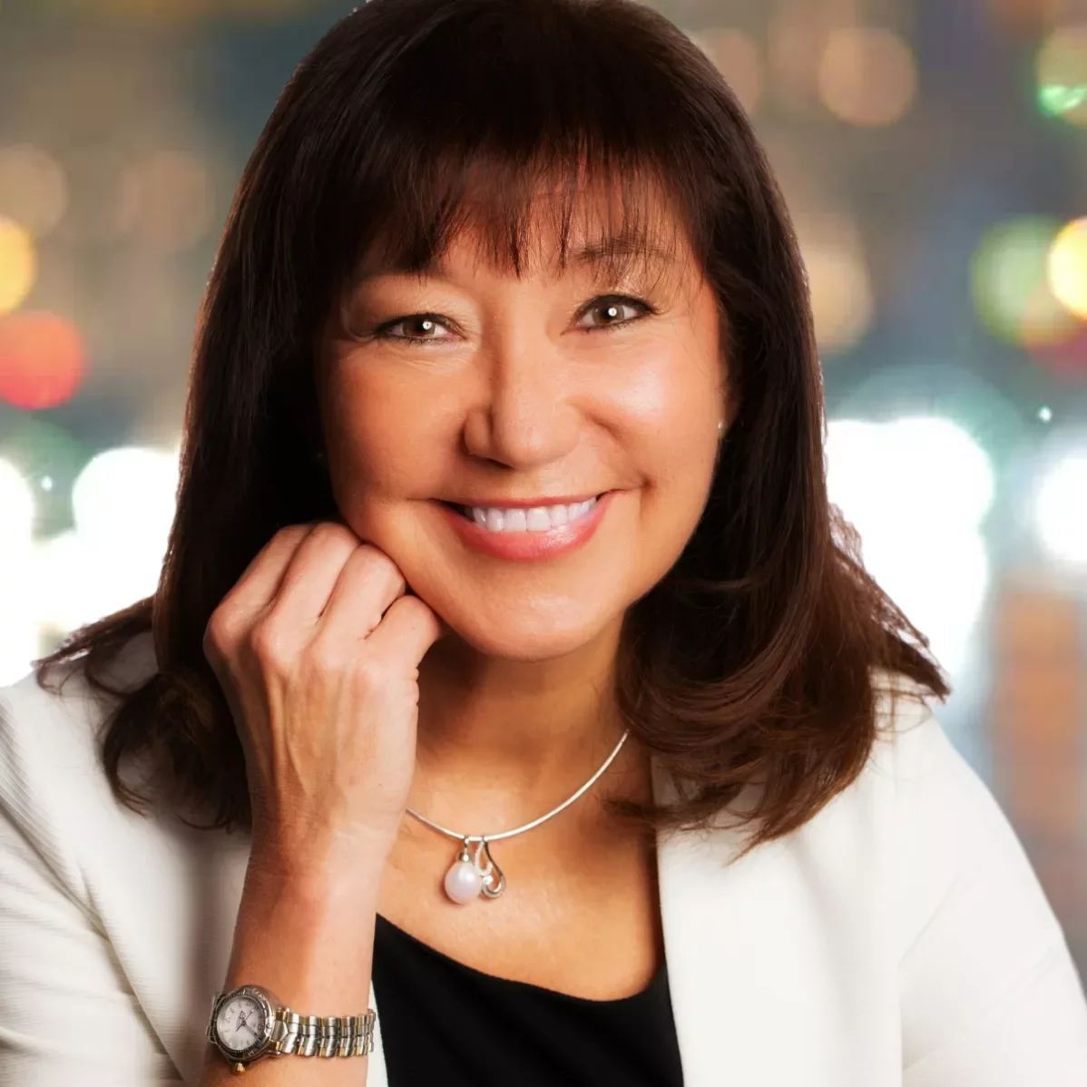 Smiling woman with dark hair and a necklace against a blurred colorful background.