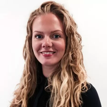 Smiling person with long curly hair, wearing a black top, against a plain background.