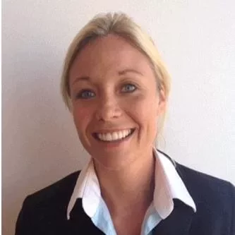 A smiling woman with blonde hair in a suit against a plain background.