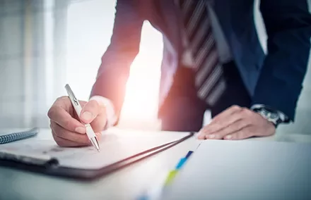 Businessperson in a suit writing in a notebook at a desk.