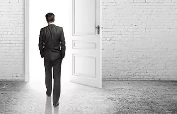 Man in a suit walking through an open door into a bright space.