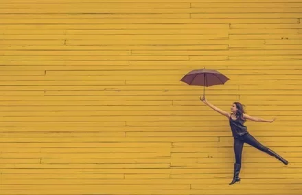 Person holding an umbrella and jumping against a yellow wooden wall.