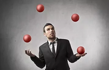 Man in a suit juggling four red balls with a focused expression.