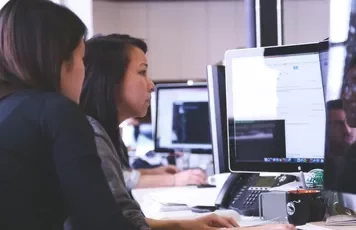Two women collaborating at a computer in an office setting.