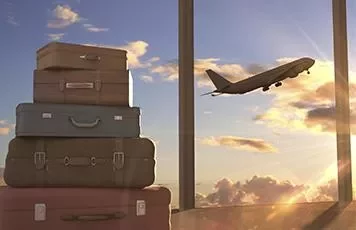 Stack of suitcases by an airport window with a plane taking off at sunset.