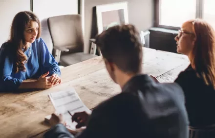 Woman in blue at a job interview with two interviewers at a wooden table.