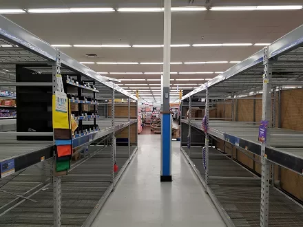 Empty store shelves with sparse items, wide aisle in a supermarket.