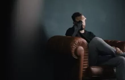 Man sitting on a leather couch with his hand on his face, looking tired.