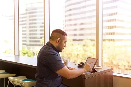 Man working on a tablet by a window with city view.
