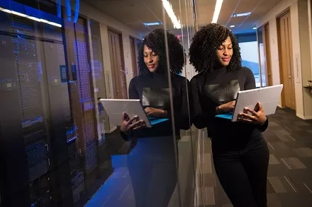 Woman in a data center hallway looking at a tablet computer.