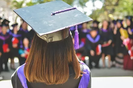 Graduate in cap and gown facing a group of fellow graduates.