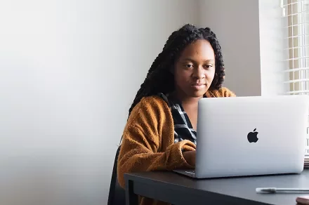 Person in a brown sweater using a laptop at a desk.