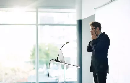 Man at podium looks stressed during a presentation.