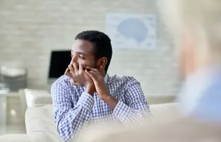 Man in a checkered shirt looking pensive in a bright room.