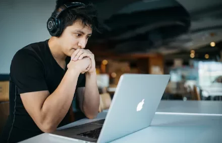 Person wearing headphones, focused on a laptop in a modern cafe.