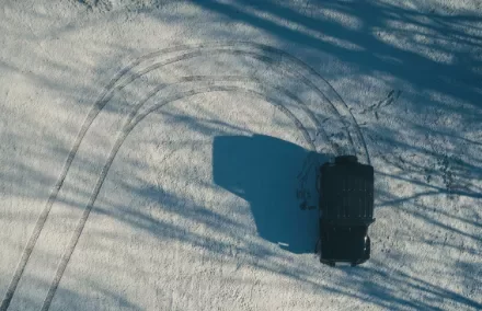 Aerial view of a black vehicle making tire tracks in the snow.