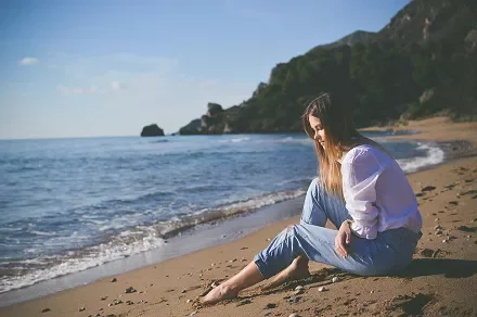 Woman sitting on a sunny beach, gazing at the ocean.