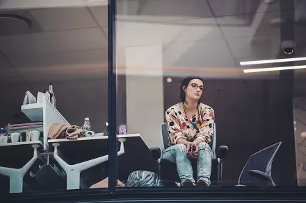 Woman in a patterned shirt sitting by a window in an office.