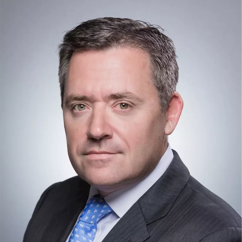 Man in a suit and blue tie against a gray background.