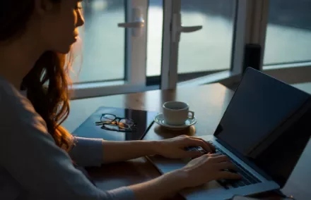 Woman typing on a laptop with a cup of coffee on a wooden table.