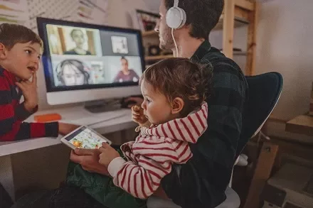 Parent working from home with children nearby during a video call.